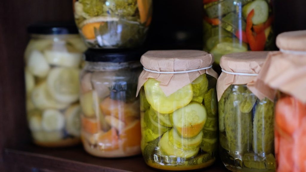 Assorted homemade pickled vegetables in glass jars on a wooden shelf.