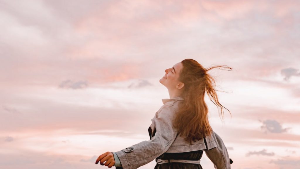 A woman joyfully embraces the sunset with arms spread in freedom, capturing serenity in nature.